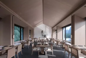 Modern restaurant interior with concrete finishes, white chairs, and large windows.
