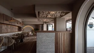 A modern restaurant interior with wooden tables and chairs, stone walls, and a combination of contemporary and rustic design 