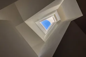 A modern vertical staircase with white walls and a blue sky at the top.