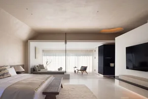 Modern minimalist bedroom with neutral materials, featuring a large bed, a sofa, and a TV.