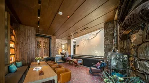 Interior of an industrial-style restaurant with wooden tables and chairs, stone fireplace, and brick walls.