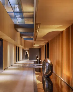 Modern interior corridor with wooden walls and concrete flooring, featuring minimalist sculptures and natural lighting.