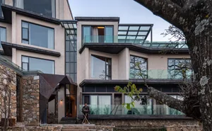 Modern residential building featuring a combination of concrete, glass, and stone exteriors, with large windows and a patio.