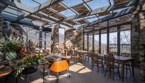 Interior design of a restaurant featuring wooden tables, glass ceiling, and stone walls.