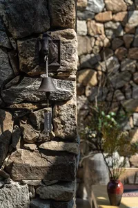 A rustic metal bell mounted on a stone wall.