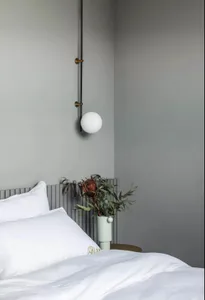A minimalist bedroom with a white bed and hanging spherical light fixture.
