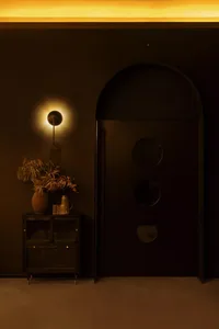 A modern entrance lamp with a metal base and a warm, ambient light, mounted on a black wall.