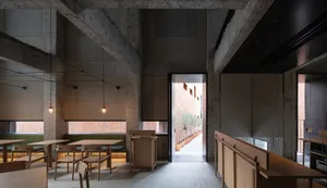 Industrial-style cafe interior with concrete walls, wooden furniture, and potted plants.