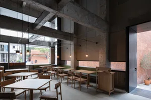 Modern coffee shop interior with wooden tables and chairs, concrete ceiling beams, and brick walls.