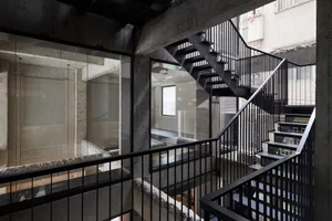 Black metal staircase with concrete walls and glass railings in an industrial-style interior.
