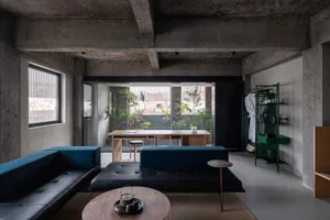 A modern industrial living room featuring a black and blue sofa, a wooden coffee table, and concrete walls.