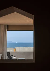 A balcony overlooking the ocean with concrete surfaces and a single white cushioned chair.