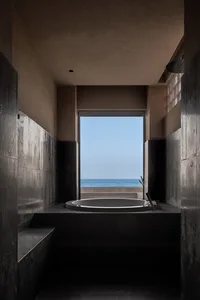 A minimalist bathroom featuring dark stone walls and floor, with a circular bathtub overlooking the ocean.