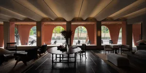 Modern minimalist hotel lounge featuring wooden furniture and leather accents, with a round table, chairs, and vases of flowe
