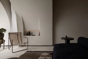 Minimalist living room with concrete walls, a black sofa, and a woven chair.