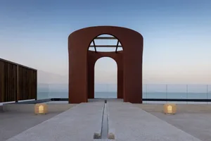 A minimalist red concrete architectural installation near the sea during dusk.