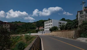 Roadside concrete and asphalt construction site with buildings and trees in the background.