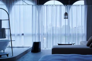 A modern residential interior with transparent curtains, glass surfaces, and minimalist furniture.