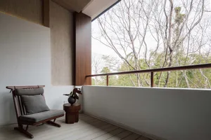 極簡住宅陽台，擺放木質椅桌與花瓶，背對大型窗戶可眺望自然景色