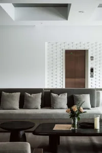 A modern living room featuring a grey sofa with pillows and a floor vase with flowers and candles.