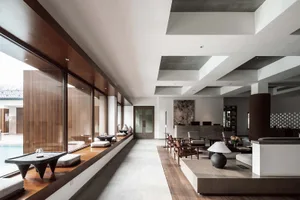A modern living room with concrete walls and a large glass window overlooking a pool.