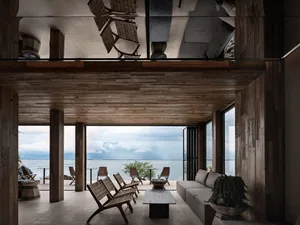 A modern living room featuring wooden walls and floor, with a view of the sea.