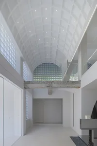 Interior view of a modern minimalist architectural space featuring white concrete walls, a glass wall, and steel details.