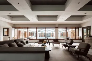 A modern minimalist living room with concrete and glass elements, featuring a large window overlooking a pool area.