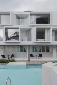 A modern minimalist poolhouse with concrete and glass exteriors and a swimming pool in front.