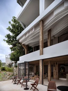A modern residential home with wooden columns and white roofing, featuring a patio area with outdoor furniture.