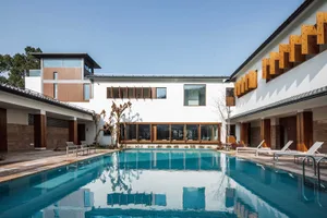 A modern residential building with a swimming pool and spa features. The exterior is made of white-rendered walls, wooden col