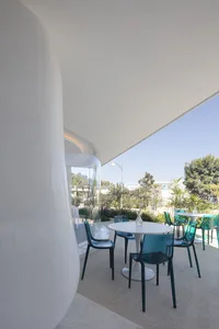 A modern restaurant terrace with glass walls, concrete surroundings, and metal chairs and tables.