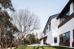 A modern residential home with a white exterior and concrete patio surrounded by trees.