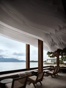 A serene restaurant interior featuring wooden furniture and canvas drapes overlooking a calm sea.