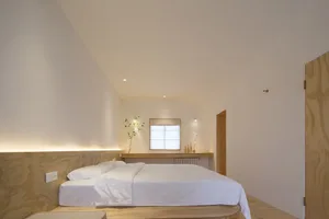 Minimalist bedroom with a white bed, wooden headboard, and minimalist decor.