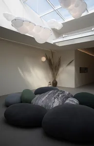 Minimalist living space with textured textiles and a concrete floor, illuminated by cloud-shaped pendant lights.