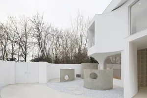 A modern minimalist white house exterior with concrete landscaping and white gravel pathway.