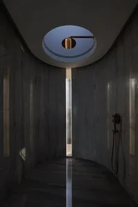 Modern bathroom with dark marble walls and floor, featuring a circular skylight and a black shower head.