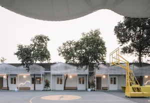 An outdoor basketball court with a glass-roofed pavilion and surrounding greenery on a clear day.