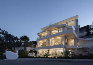 A modern house with a glass exterior, illuminated at dusk.