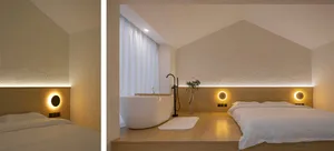 A modern minimalist bedroom with a wooden platform bed, white bedding, a freestanding bathtub, and soft lighting.