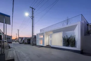 Modern minimalist house with concrete frame and metal railings, illuminated by a streetlight at dusk.