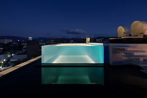 Modern rooftop swimming pool with glass walls and illuminated interior.