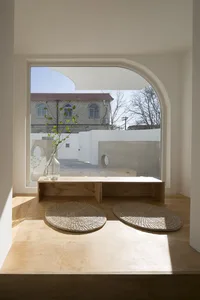 A serene corner of a home studio illuminated by natural light, featuring a wooden bench, woven baskets, and a vase with green