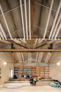 People sitting on wooden benches in a library with industrial-style exposed beams and high ceiling.