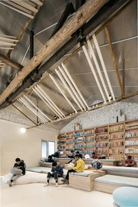 人們在現代圖書館閱讀書籍，露出木樑、金屬裝飾與混凝土地板。