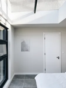 A minimalist bedroom featuring a concrete floor and walls, with a white bed and skylight.