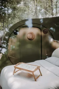 A minimalist bedroom with a white bed and wooden tray on top of it, set against a backdrop of a transparent dome structure vi