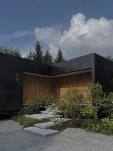A modern minimalist house featuring black walls, wooden paneling, and concrete steps leading up to it.