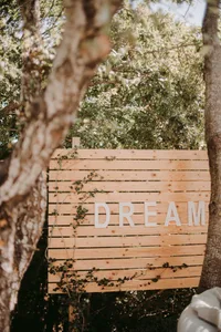 A minimalist wooden outdoor hanging signage with a wreath design.